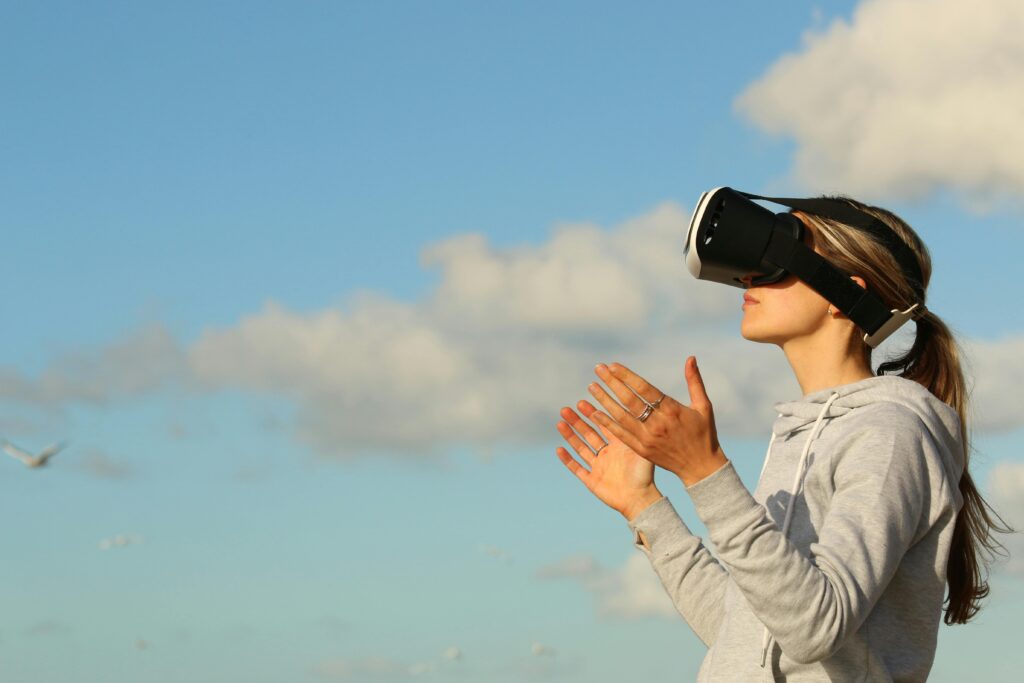 Une femme portant un casque de réalité virtuelle, mains levées, ciel bleu en arrière-plan.