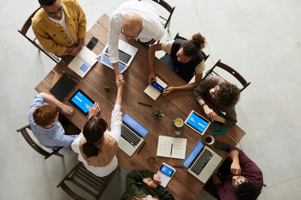 Personnes en réunion autour d'une table, avec ordinateurs portables et tablettes.
