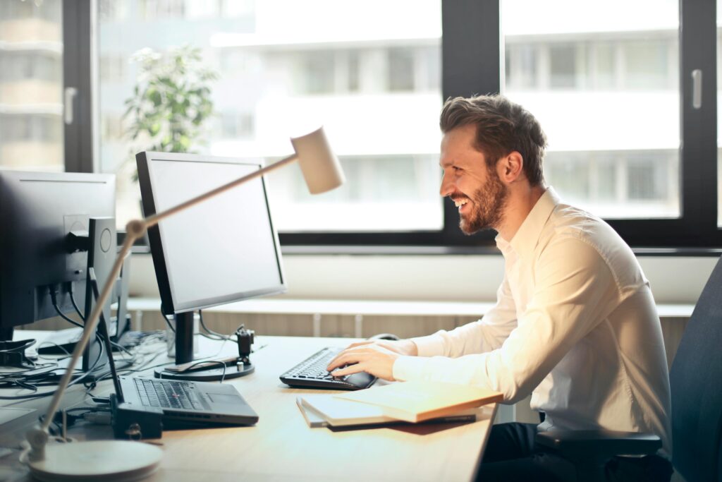Homme souriant travaillant à un bureau avec ordinateur et lampe de bureau.